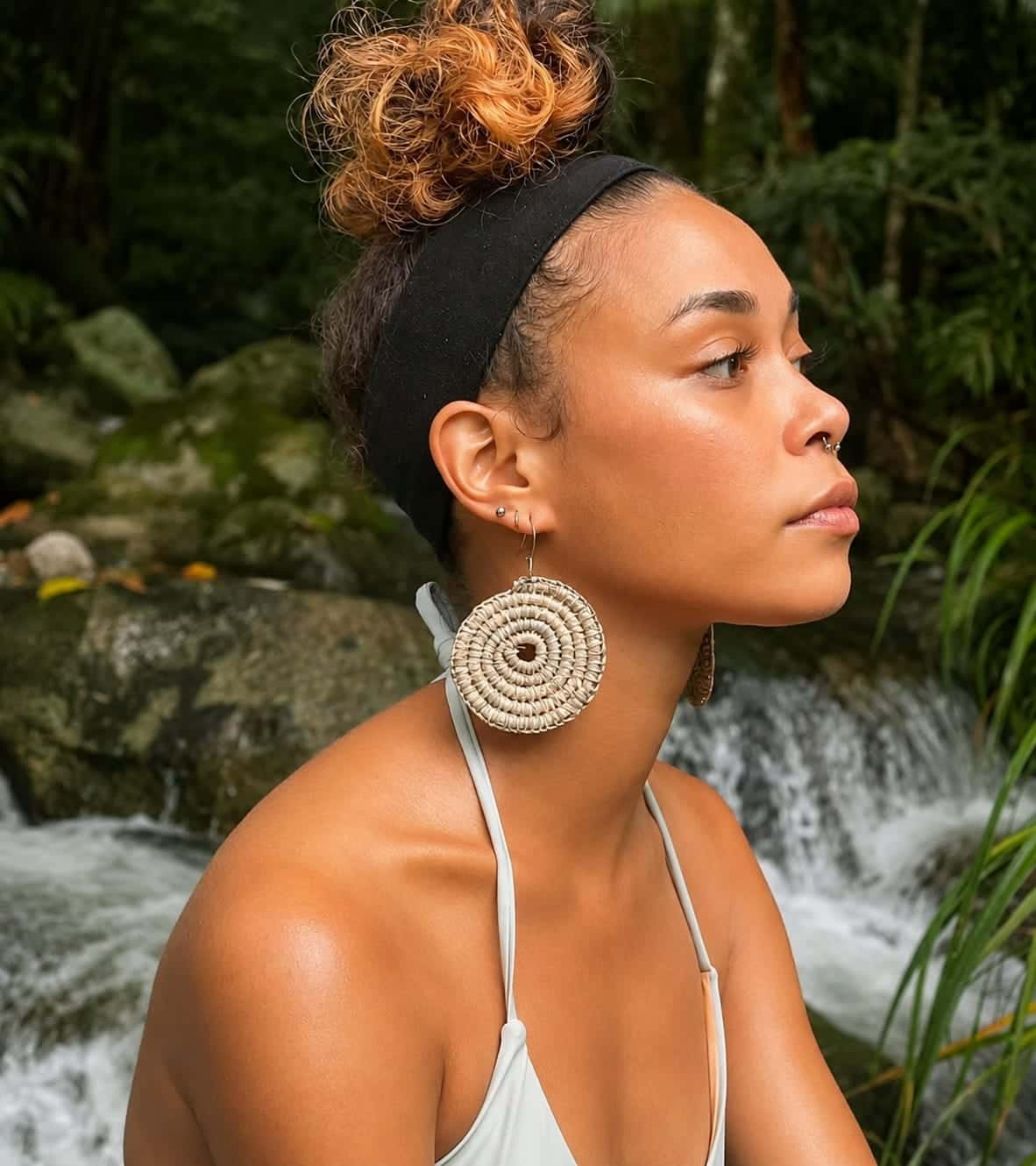 Woman wearing large circular woven earrings beside a rainforest waterfall.