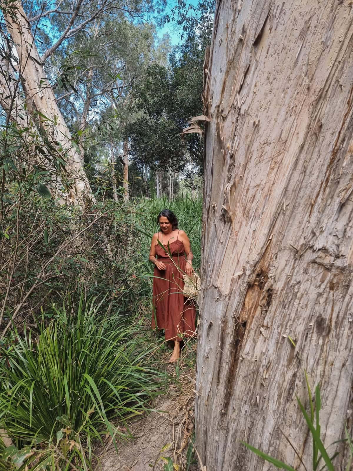 Julie walking among paperbark trees and native grasses on Country.