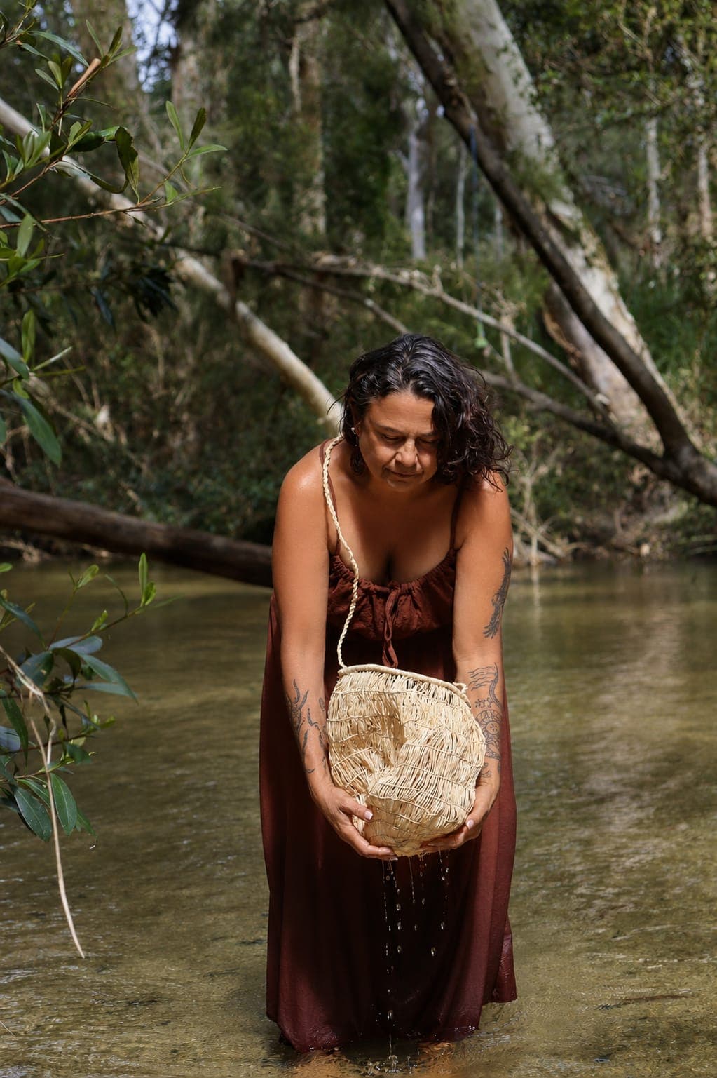 Julie standing in clear creek water beneath paperbark trees.