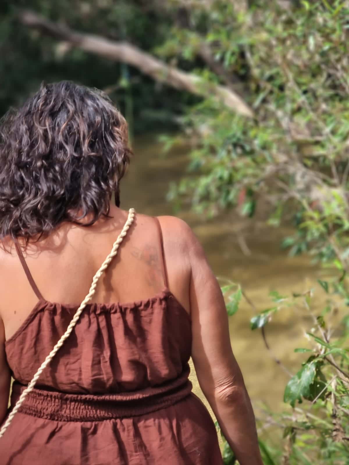 Julie walking towards a quiet creek on Country with a woven fibre bag.