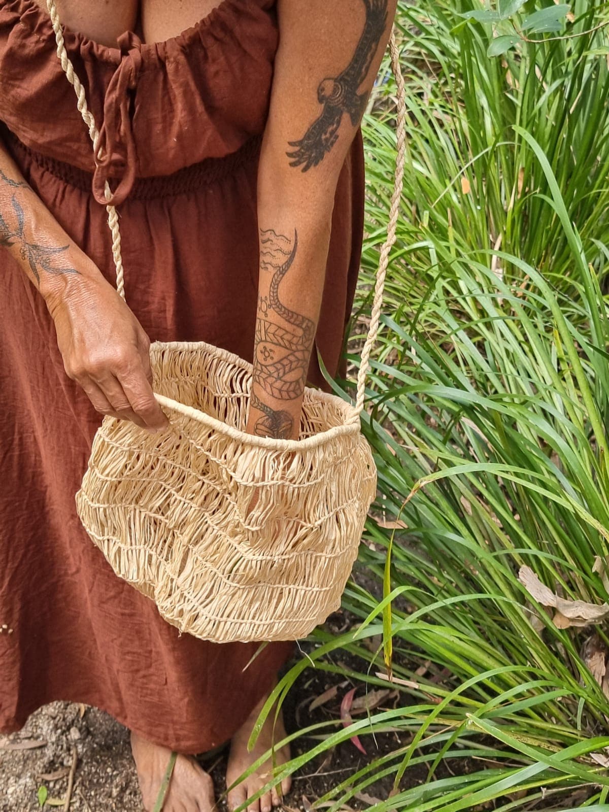 Julie holding a handwoven natural-fibre bag among creek-side grasses.