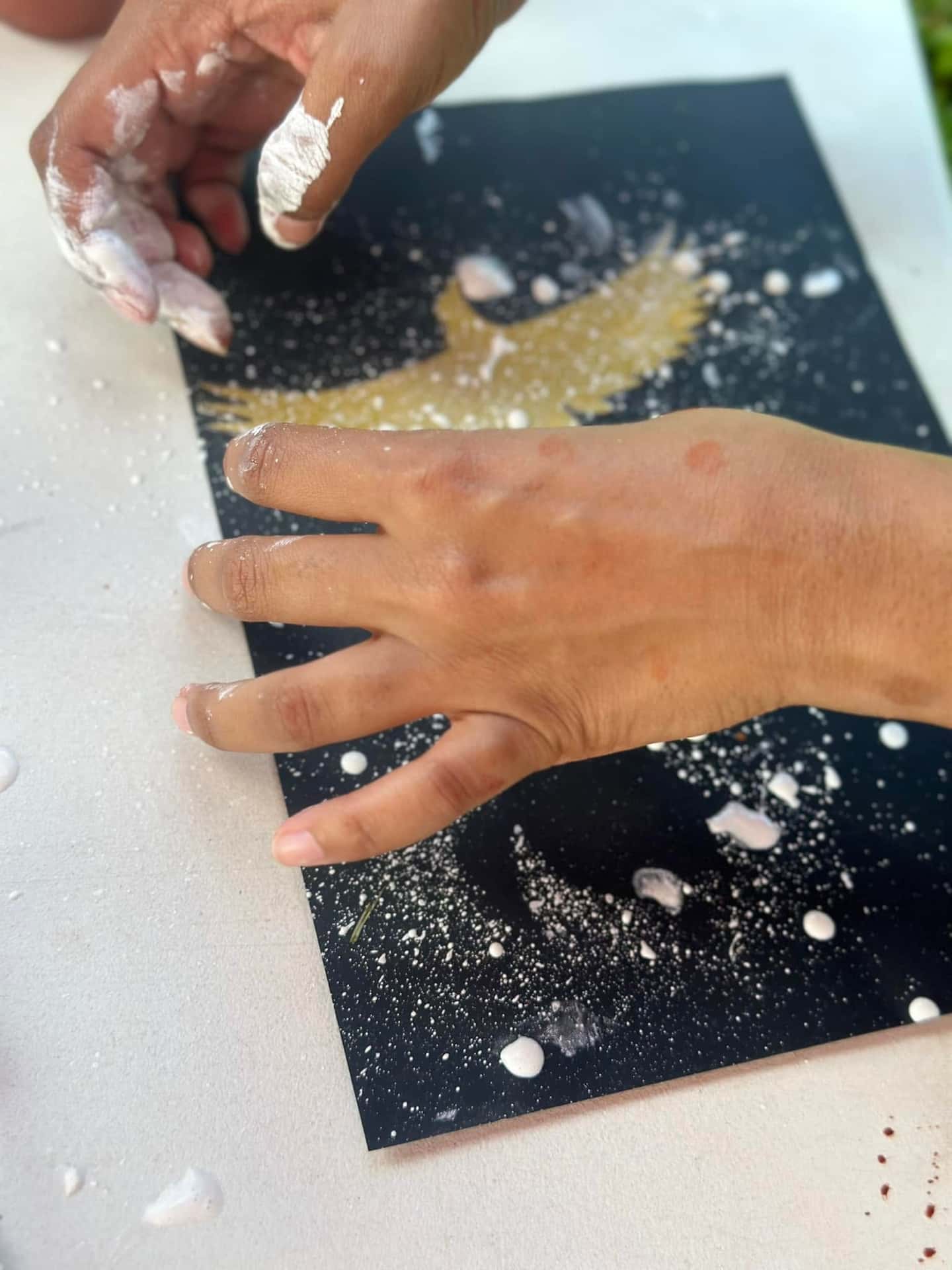 Hands working with ochre pigments on a black artwork during a workshop.
