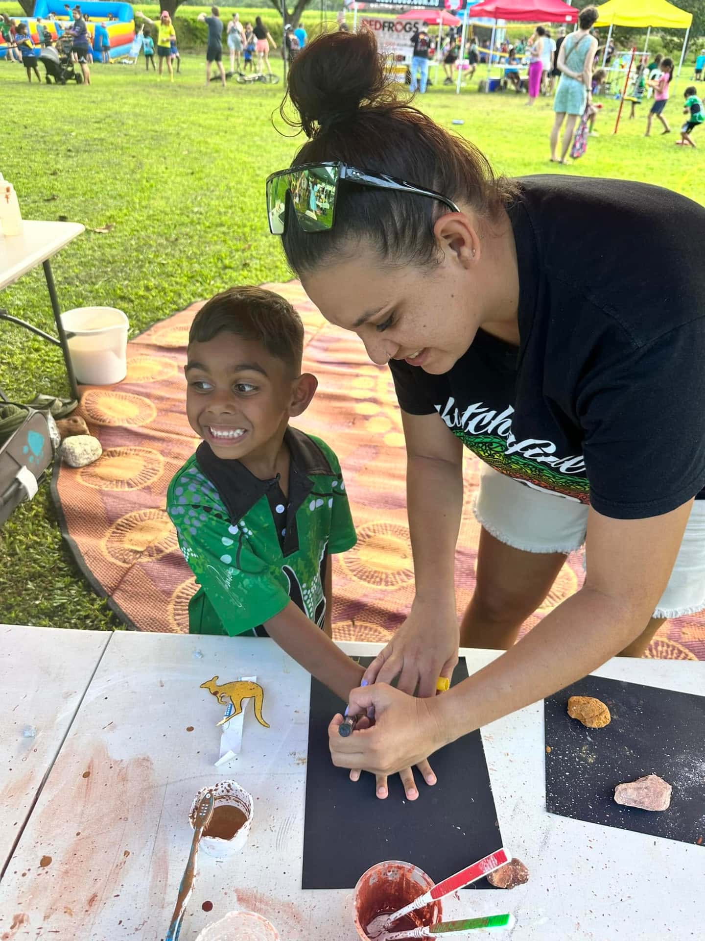 A child and adult creating ochre artwork together at an outdoor workshop.