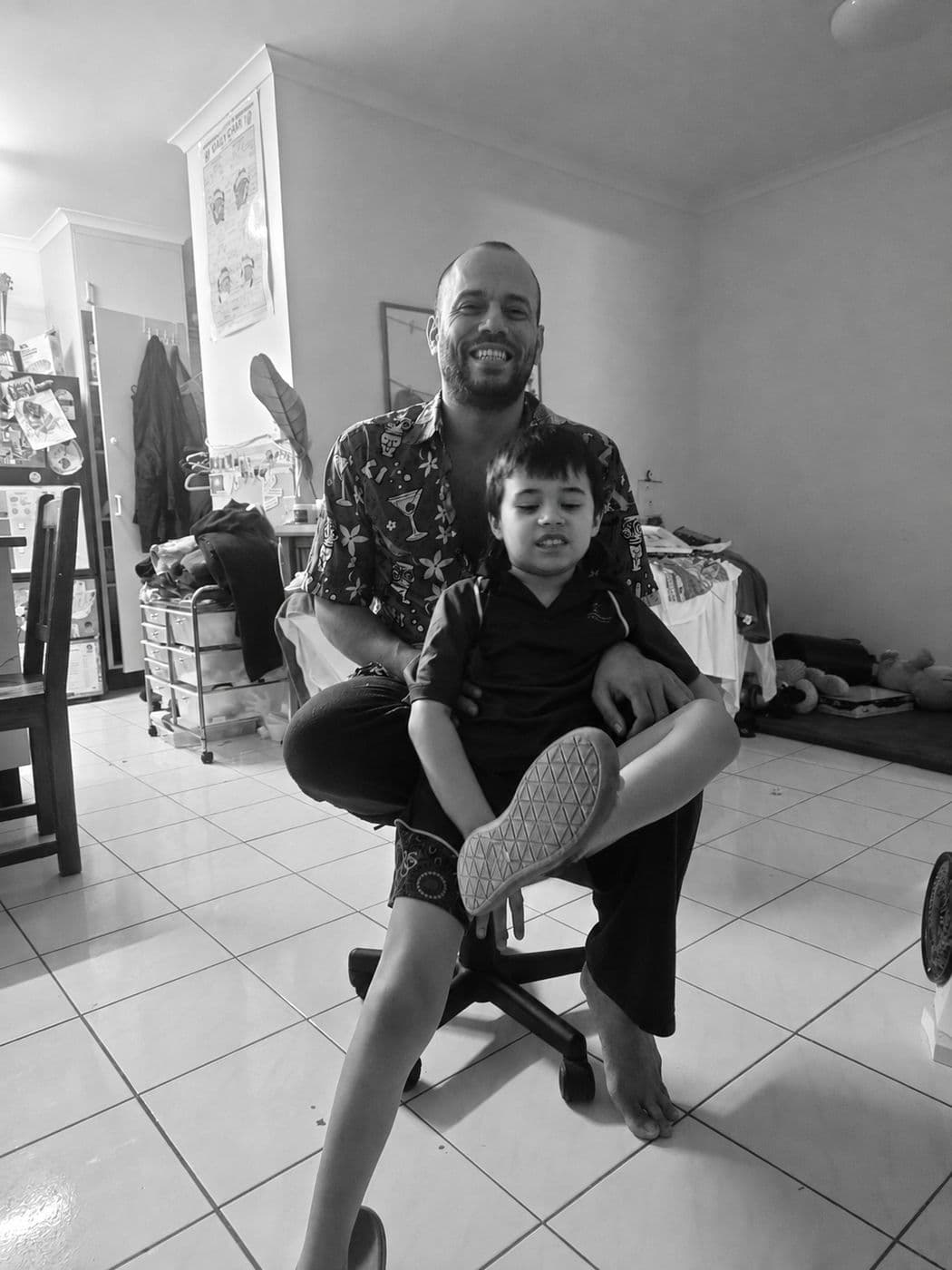Black-and-white family photo: a smiling man seated with a young child on his lap at home.